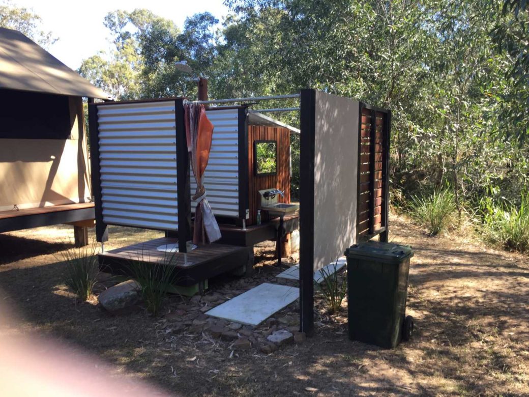 Open-air outdoor shower facility surrounded by natural timber screening at Hangar O
